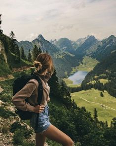 a woman standing on top of a lush green hillside next to a lake and mountains