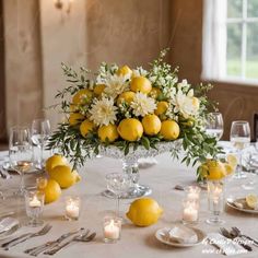 a centerpiece with lemons and white flowers sits on a table in front of candles