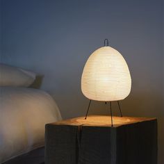 a white lamp sitting on top of a wooden block next to a night stand with a bed in the background