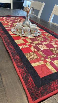 the table is set with two cups and a silver tray on it, along with an ornately designed runner