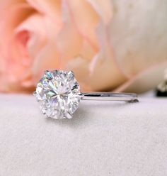 a diamond ring sitting on top of a white surface next to a pink rose and flower