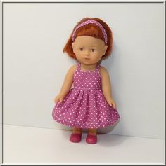 a doll with red hair wearing a pink polka dot dress and headband standing against a white wall