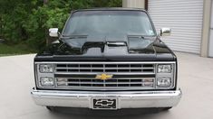 the front end of a black truck parked in a driveway next to a garage door