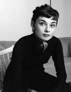 a woman sitting on top of a couch next to a white chair and looking at the camera