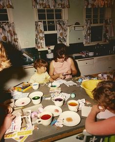 a group of people sitting around a kitchen table with bowls and plates on top of it