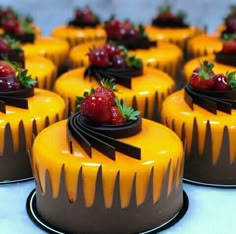 several cakes with chocolate icing and strawberries on top are lined up in rows