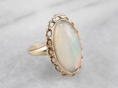 "The framework of this ring is a simple filigree, with a scalloped profile. The openwork allows plenty of light into the center of the stone, allowing the bright orange and green to really shine through. The bezel not only holds the stone it also protects the cabochon from wear, and still allows the opal to glow! Metal: 14K Yellow Gold Gem: Opal Gem Measurements: 15.2 x 8.0 mm, Oval Ring Size: 2.50 Marks: \"14K\" Stamped on the inside band SKU #: AFTPK11K Each piece has been identified and grade Fine Jewelry Wedding Rings With Fluted Bezel, Wedding Rings With Fluted Bezel, Formal Oval Jewelry With Fluted Bezel, Heirloom Moonstone Wedding Ring With Polished Finish, Oval Moonstone Ring For Wedding With Intricate Design, Oval Moonstone Wedding Ring With Intricate Design, Elegant Oval Filigree Ring With Cabochon, Oval Opal Ring With Intricate Design For Wedding, Heirloom Style Oval Filigree Ring With Cabochon