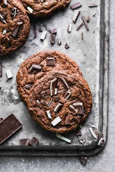 three chocolate cookies on a baking sheet with broken pieces