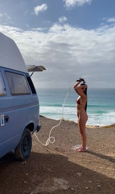 a woman standing in front of a van next to the ocean