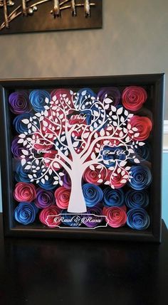 a paper quilled tree is displayed in a shadow box on a black table with blue, red and white spirals