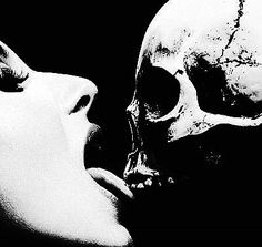 a black and white photo of a woman kissing a skull