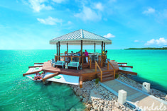 people are sitting at the end of a dock with an umbrella over it and some rocks