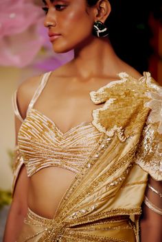 The flower patch on the shoulder seems like it is blooming from the joy of the season. The draped saree made with lightweight fabric materializes the concept of a fairy. The gold saree is embellished with beadwork and applique flowers all around to appear as if standing amongst flowers. Cold shoulder style blouse with back hook Pre-draped saree with a flower patch on the shoulder accentuated with beads and sequins embroidery. Metal zip on the saree. From Moledro’s Taabir collection. DELIVERY TIM Beads And Sequins Embroidery, Gold Saree, Applique Flowers, Draped Saree, Cold Shoulder Styles, Drape Saree, Trendy Blouse, Sari Blouse, Trendy Blouses