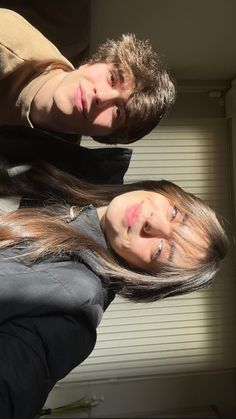 two people standing next to each other in front of a window with blinds on it