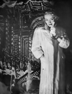 an old photo of a woman in a fur coat standing next to a large painting