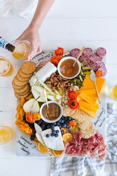 a platter filled with cheese, crackers, fruit and meats next to two glasses of beer