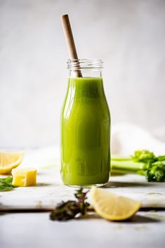 a green smoothie in a mason jar with a straw and some lemon wedges