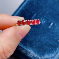 a woman's hand is holding a ring with three stones on it and the other side has a blue velvet box behind it