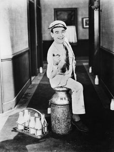 an old black and white photo of a boy sitting on top of a barrel