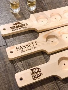 three glasses are sitting on a table with wooden paddles and labels that say bassett brewery