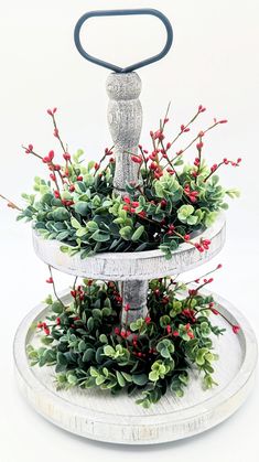 a three tiered tray with red berries and greenery on it, holding a metal handle