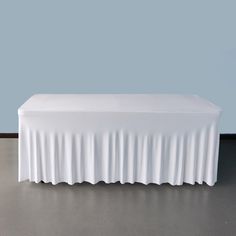 a white table with a long skirt on it's end and a light blue wall in the background