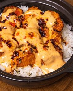 chicken with gravy on top of rice in a black crockery dish