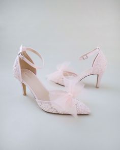 a pair of pink high heeled shoes with a bow on the ankle and lace detailing