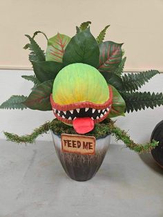 a planter with a fake monster head sitting on top of it next to a sign that says feed me