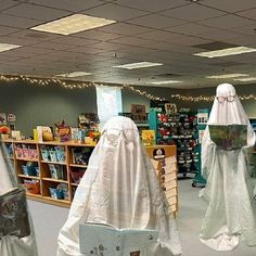 three white ghost statues are in the middle of a book store's display area