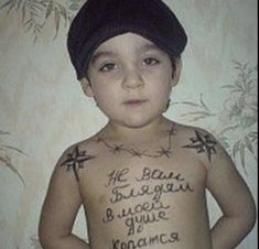 a young boy with tattoos on his chest and arms is standing in front of a wall