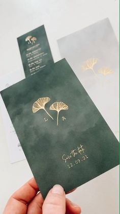 a person holding up a green wedding card with gold foil flowers on the front and back