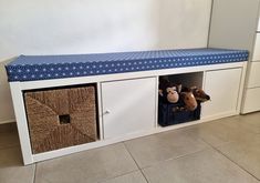 two stuffed animals sit on top of a white bench with baskets underneath it and the seat is covered in blue fabric