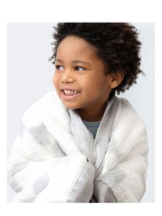 a young child with curly hair wearing a white jacket and smiling at the camera while wrapped in a blanket