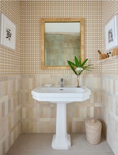 a white pedestal sink sitting under a mirror next to a vase with flowers in it