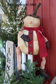 an old fashioned snowman hanging on the side of a red door in front of a christmas tree