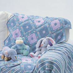 two stuffed animals sitting on top of a couch next to a blanket and pillow cover