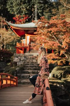 a woman sitting on the edge of a bridge in front of a red pagoda and trees