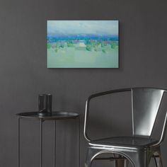 a chair and table with a painting on the wall above it in a living room