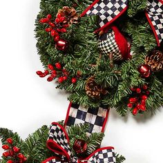 two christmas wreaths with red bows and pine cones on them, hanging from a white wall