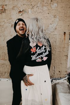 a man and woman standing next to each other in front of a wall with graffiti on it