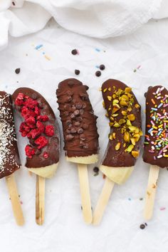 five chocolate covered popsicles with sprinkles and toppings lined up on top of each other