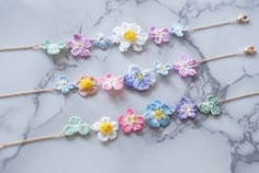 four crocheted flowers are arranged on a marble countertop, with gold chains