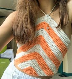 a woman wearing an orange and white crochet tank top holding a cell phone