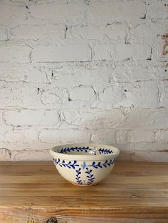 a blue and white bowl sitting on top of a wooden table next to a brick wall