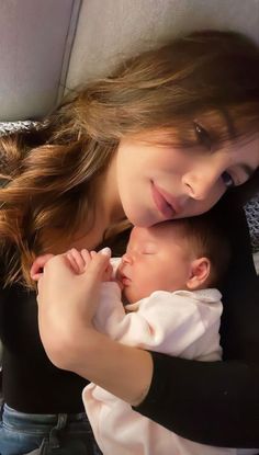 a woman holding a baby in her arms while laying on top of a car seat