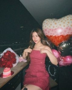 a woman in a red dress sitting at a table surrounded by balloons and other decorations