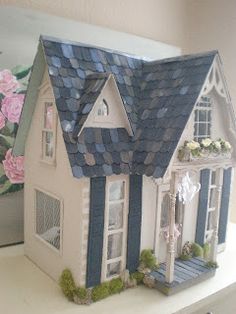 a doll house with blue shingles and white trim on the roof is sitting on a shelf