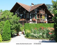 an old style house surrounded by greenery and flowers on a sunny day in the mountains