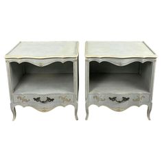 two white nightstands with gold trimming on the top and one has an open drawer